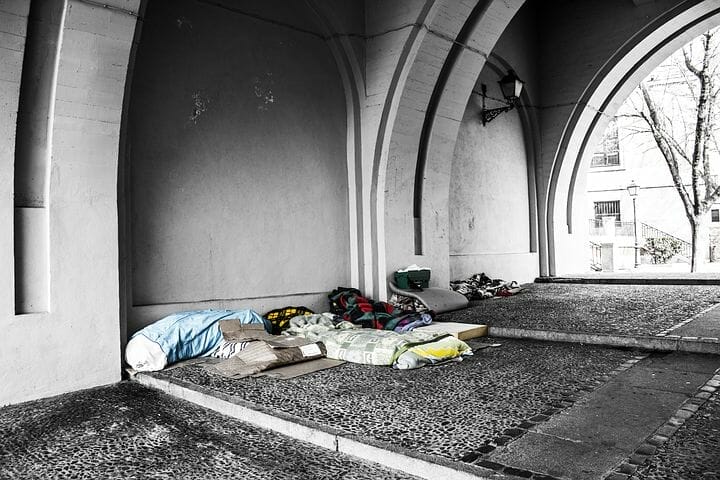 A homeless person sleeping under an arch in a black and white photo, depicting vulnerability and poverty.