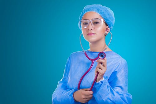 A medical student on clinical rotation holds a stethoscope in a blue background.